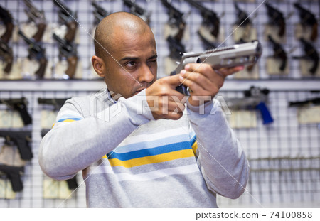 Focused latin american man aiming with pistol in gun shop 74100858