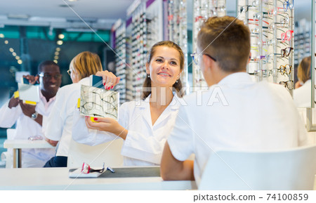 Boy choosing glasses and ophthalmologist holding mirror Boy choosing glasses and ophthalmologist holding mirror 74100859