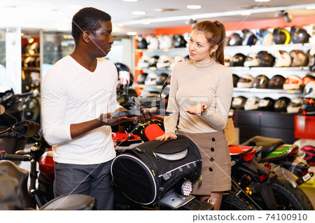 Positive young couple looking for new duffel bag for motorcycle in shop of moto equipment 74100910