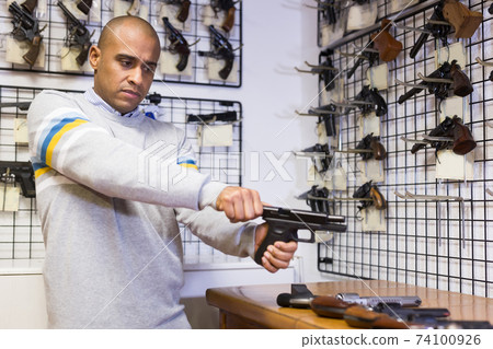 Confident latin american man racking pistol slide in shop Confident latin american man racking pistol slide in shop 74100926