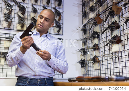 Hispanic man inserting magazine in pistol grip at gun shop 74100934