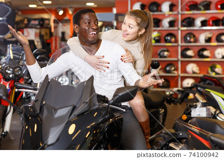 cheerful man and woman posing on new motorcycle in shop cheerful man and woman posing on new motorcycle in shop 74100942