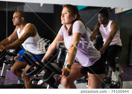 Woman training on stationary bike in gym Woman training on stationary bike in gym 74100944