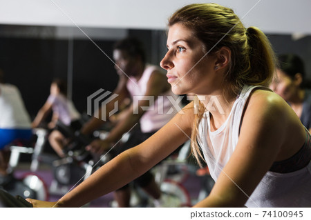 Woman training on stationary bike in gym Woman training on stationary bike in gym 74100945