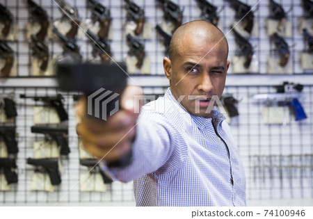 Focused latin american man aiming with pistol in gun shop Focused latin american man aiming with pistol in gun shop 74100946