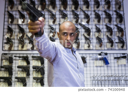 Focused latin american man aiming with pistol in gun shop 74100948