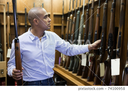 Portrait of owner of hunting shop standing with shotgun indoors 74100958