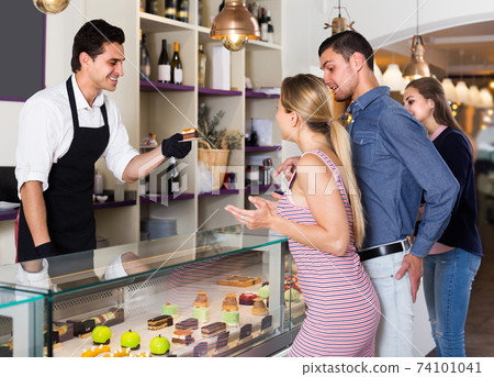 Male with two female are choosing delicious cakes from showcase Male with two female are choosing delicious cakes from showcase 74101041