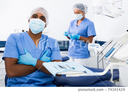 Qualified dentist standing in blue uniform in dental office 74101429