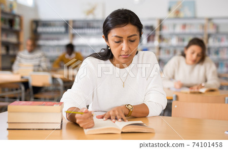 Concentrated hispanic woman reading books in public library 74101458