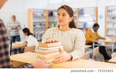 Young adult woman returning books at library 74101603