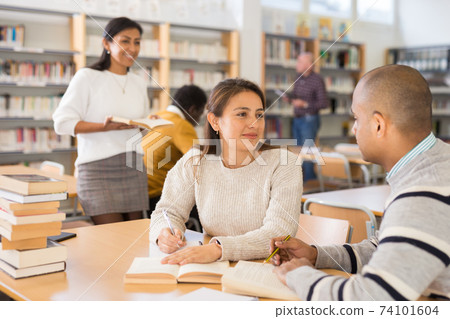 Positive hispanic man and woman reading books in library Positive hispanic man and woman reading books in library 74101604