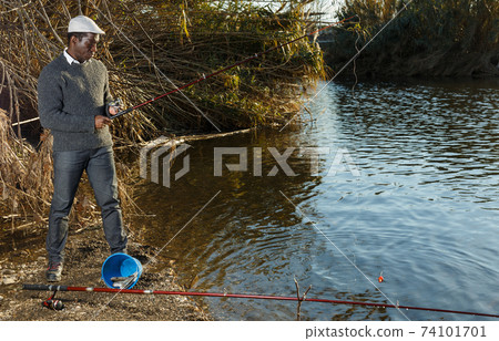 Afro fisherman standing near river Afro fisherman standing near river 74101701