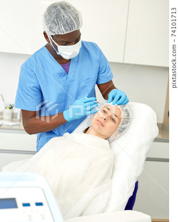 Woman client and doctor during beauty facial injections in medical esthetic office 74101713