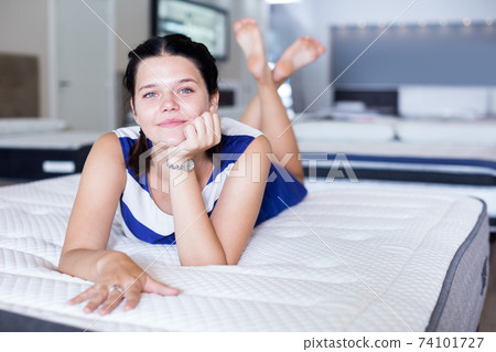 Female lying on soft mattress and smiling in store Female lying on soft mattress and smiling in store 74101727
