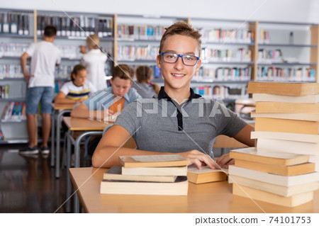 Schoolboy sitting with stacks of books in school library Schoolboy sitting with stacks of books in school library 74101753
