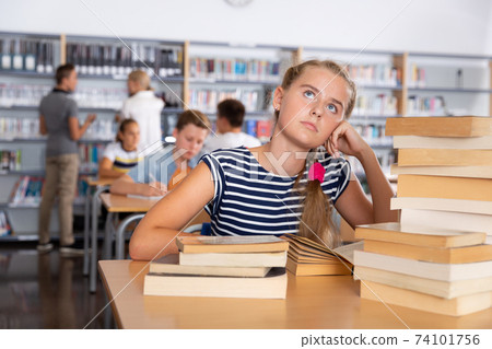 Smiling schoolgirl sitting at table with stacks of books Smiling schoolgirl sitting at table with stacks of books 74101756