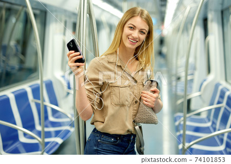 Happy blonde listening to music on headphones in a subway car Happy blonde listening to music on headphones in a subway car 74101853
