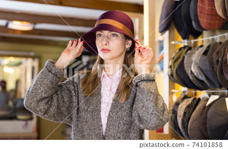 Woman trying on hat during shopping Woman trying on hat during shopping 74101858