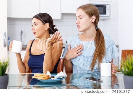 Portrait of unhappy girl friends discussion while drinking tea in home 74101877