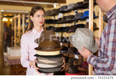 Salesgirl offering hats to man 74101879