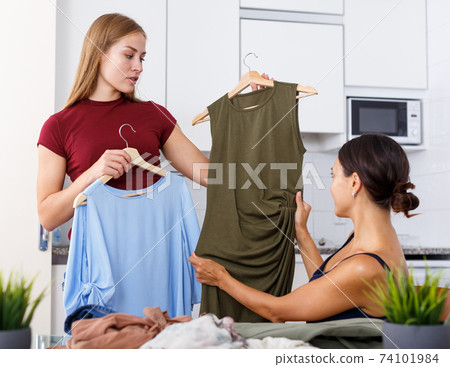 Smiling young women friends chatting and looking at clothes together Smiling young women friends chatting and looking at clothes together 74101984