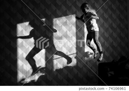 Girl jumping in front of the wall and her shadow is on the wall Girl jumping in front of the wall and her shadow is on the wall 74106961