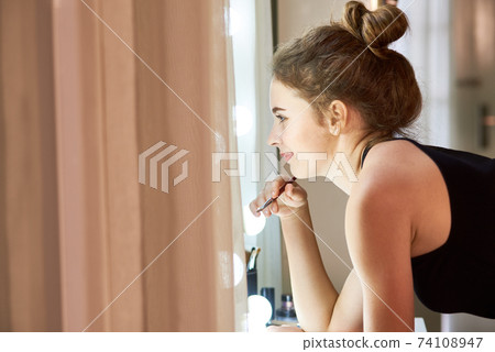 Young woman applying liquid lipstick 74108947