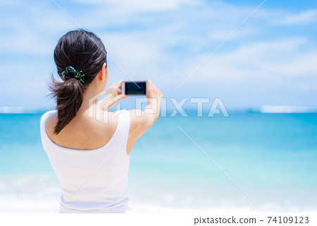 A woman taking a picture of the sea with a smartphone 74109123