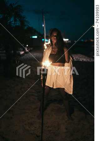 Young woman with torchlight on the beach at night 74109983