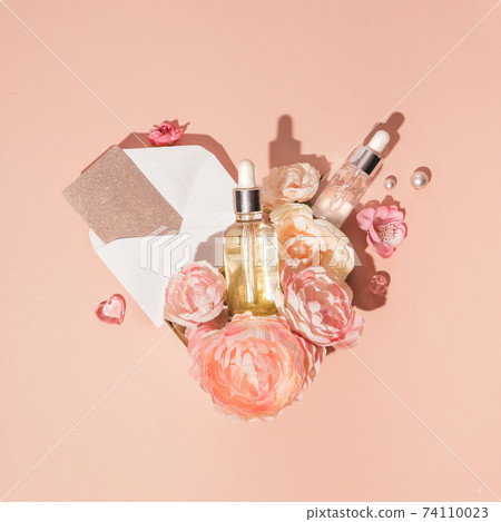 Composition in the shape of heart of natural cosmetics, skin care serums combined with flowers and gift card, peach pastel background 74110023