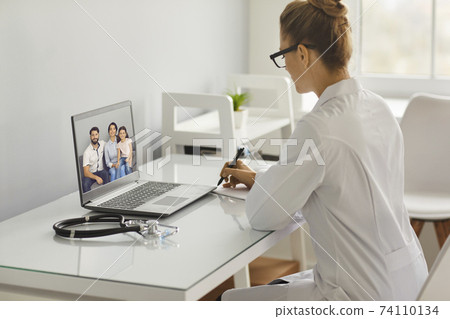 Young woman doctor therapist in uniform making notes during online consultation with family Young woman doctor therapist in uniform making notes during online consultation with family 74110134