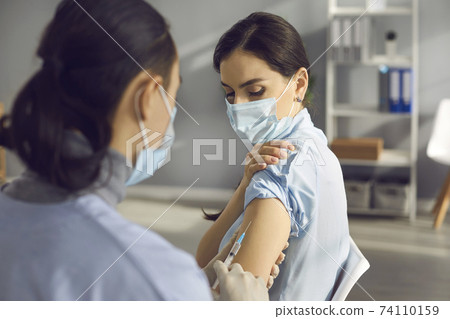 Young woman in medical face mask getting vaccine injection during infection outbreak 74110159