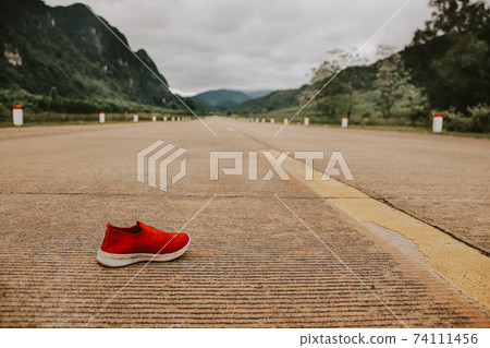 Conceptual photo of a single red shoe left behind in the middle of a deserted highway showing concept of despair, depression, mental health issues and life 74111456