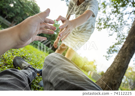 Asian child girl helping to support the man to stand up from on the grass after falling down because of an accident, playing with her at park,daughter pulling hand and give encouragement her father 74112225
