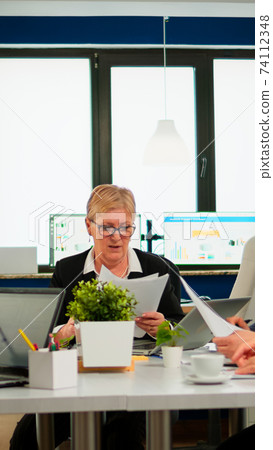 Secretary bringing coffee and meeting documents while team planning financial strategy Secretary bringing coffee and meeting documents while team planning financial strategy 74112348