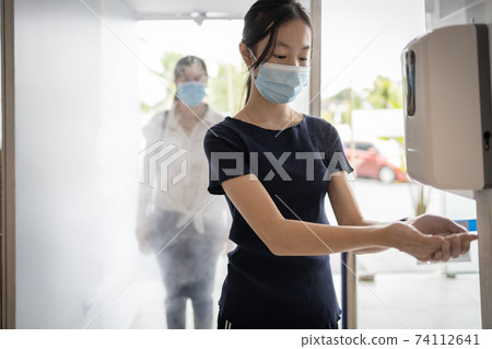 Child girl wear face mask using automatic alcohol gel dispenser,spraying on hand for disinfecting,woman in the automatic disinfection tunnel,check point for COVID-19,cleaning,safety under Coronavirus Child girl wear face mask using automatic alcohol gel dispenser,spraying on hand for disinfecting,woman in the automatic disinfection tunnel,check point for COVID-19,cleaning,safety under Coronavirus 74112641