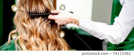 Hairdresser combing wavy hair of woman Hairdresser combing wavy hair of woman 74113362