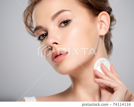 Beautiful face of a young Caucasian woman with a cotton pad in her hand, isolated. Pretty white model takes care of her face. Removing makeup with a cotton swab Beautiful face of a young Caucasian woman with a cotton pad in her hand, isolated. Pretty white model takes care of her face. Removing makeup with a cotton swab 74114116