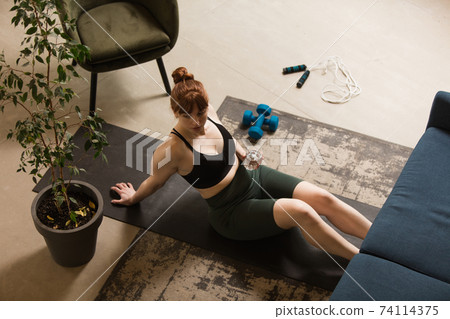 Young woman exercising fitness, aerobic, yoga at home, sporty lifestyle. Getting active during lockdown, quarantine. Home gym. 74114375