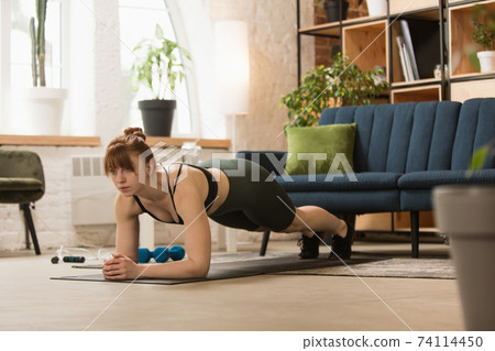 Young woman exercising fitness, aerobic, yoga at home, sporty lifestyle. Getting active during lockdown, quarantine. Home gym. Young woman exercising fitness, aerobic, yoga at home, sporty lifestyle. Getting active during lockdown, quarantine. Home gym. 74114450