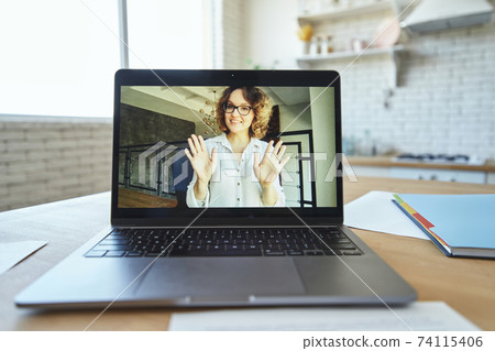 Close up of laptop screen with happy female teacher smiling and waving goodbye during video call, having online lesson Close up of laptop screen with happy female teacher smiling and waving goodbye during video call, having online lesson 74115406