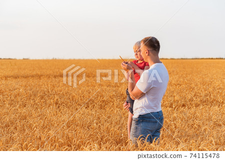 Father holding son in arms on background field of ripe wheat. Weekend in countryside Father holding son in arms on background field of ripe wheat. Weekend in countryside 74115478