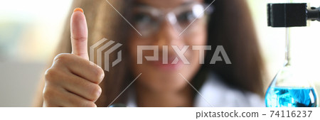 Researcher with microscope and flask holds thumb up. 74116237