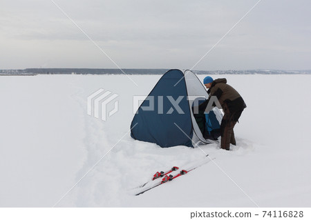 Man in  suit for winter fishing putting up a tent  74116828