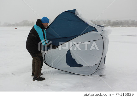 Man is putting up a tent on a frozen river Man is putting up a tent on a frozen river 74116829