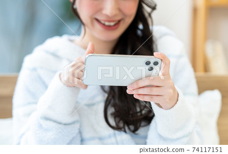 一個年輕的女人，看著她的智能手機上的視頻 74117151