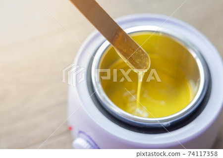 Yellow hot liquid wax for depilation on a wooden stick. The concept of depilation, beauty, skin care Yellow hot liquid wax for depilation on a wooden stick. The concept of depilation, beauty, skin care 74117358