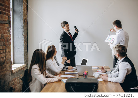 Male speaker giving presentation in hall at workshop. Audience or conference hall. Participants, co-workers listening at the table. Male speaker giving presentation in hall at workshop. Audience or conference hall. Participants, co-workers listening at the table. 74118213