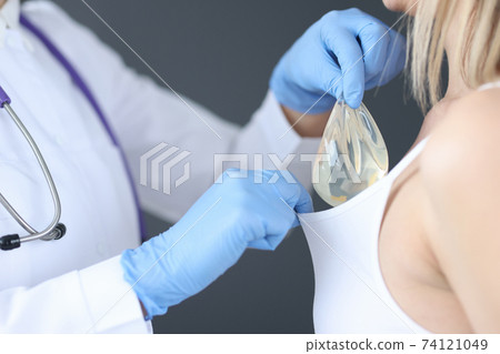 Doctor inserting breast implant under patients sink closeup 74121049